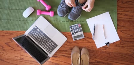 A blend of personal wellness and professional productivity items — featuring a yoga mat, sneakers, laptop, calculator, and office supplies laid out on a hardwood floor.